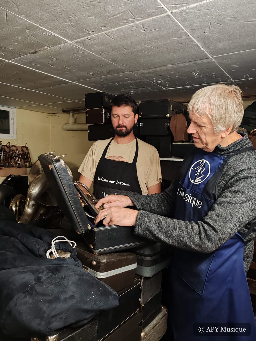 Amaury et Jean-Michel Plecety ensemble à l'atelier, penchés sur un étui de trompette entouré de cuivres